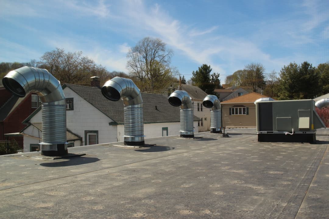 Rooftop with multiple ventilation pipes against a clear blue sky.