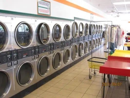Modern laundromat featuring multiple silver dryers and a clothing rack for customers.